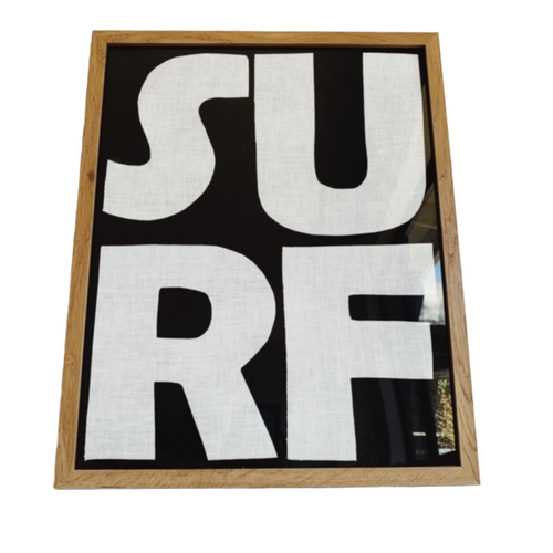 Framed textile art with black background and white mod lettering that spells out SURF with SU  on top and RF on bottom, Natural oak frame.