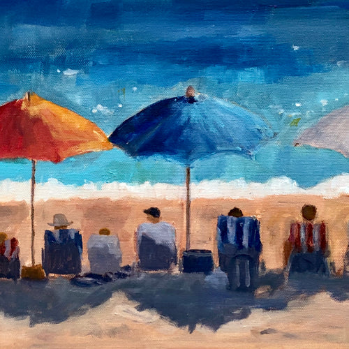 a row of people on the beach under the red, white and blue umbrellas sitting in beach chairs.  Some chairs have striped towels.