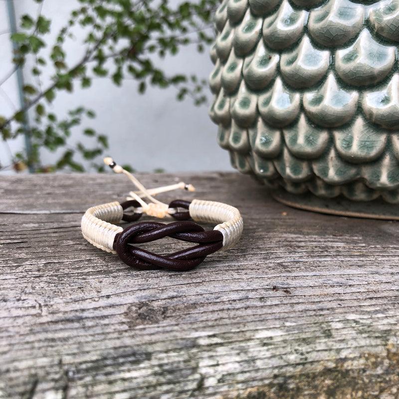 The cream  and brown Macrame Playa Leather Men's Bracelets are handwoven, made with sturdy waxed cotton that is wrapped around a double leather intertwined cord, and closed with an Italian waxed-cord clasp. This bracelet has a large knot in the center.