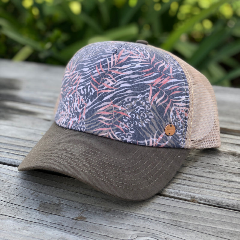 The Gidget trucker cap, by Kooringal has a tan mesh back, charcoal brim, and a charcoal and pink tropical print.