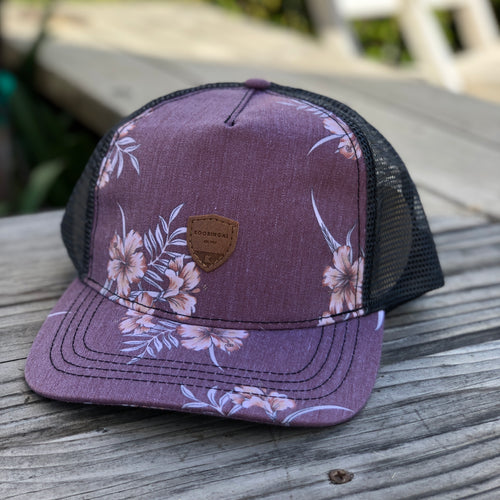The Coastal men's trucker hat has a mesh back, snap back adjustable, and maroon color palette with tropical hibiscus.