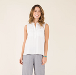 Front view of a female model wearing the Carve Designs Frankie Tank in cloud solid, or white. Top has a relaxed fit, button front, placket chest pockets, and shirttail hem with vents. Paired with grey wide leg pants.