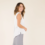 Side view of a female model wearing the Carve Designs Frankie Tank in cloud solid, or white. Top has a relaxed fit, button front, placket chest pockets, and shirttail hem with vents. Paired with grey wide leg pants.