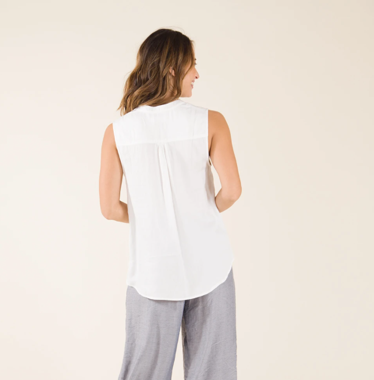 Back view of a female model wearing the Carve Designs Frankie Tank in cloud solid, or white. Top has a relaxed fit and shirttail hem with vents. Paired with grey wide leg pants.