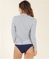 Back view of a female model wearing Carve Designs Cruz rashguard in dash stripe, or navy blue and white horizontal stripes. 1/2 zip with 1.5" standup collar and adjustable side ruching. Paired with bikini bottoms.