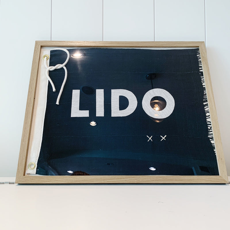Framed navy flag with grommets and tie, featuring ivory lettering that spells LIDO; includes hand embroidered X design at bottom corner