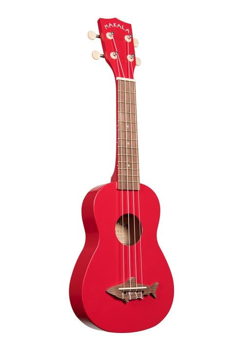 Red Makala brand ukulele with wooden shark bridge and white background. 