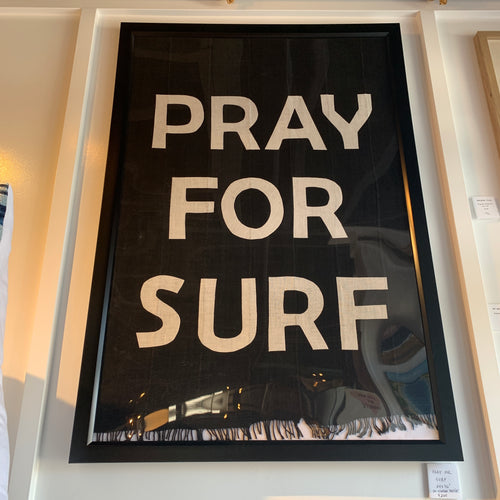Framed textile artwork with dark cloth background and ivory lettering spelling out PRAY FOR SURF in capital letters